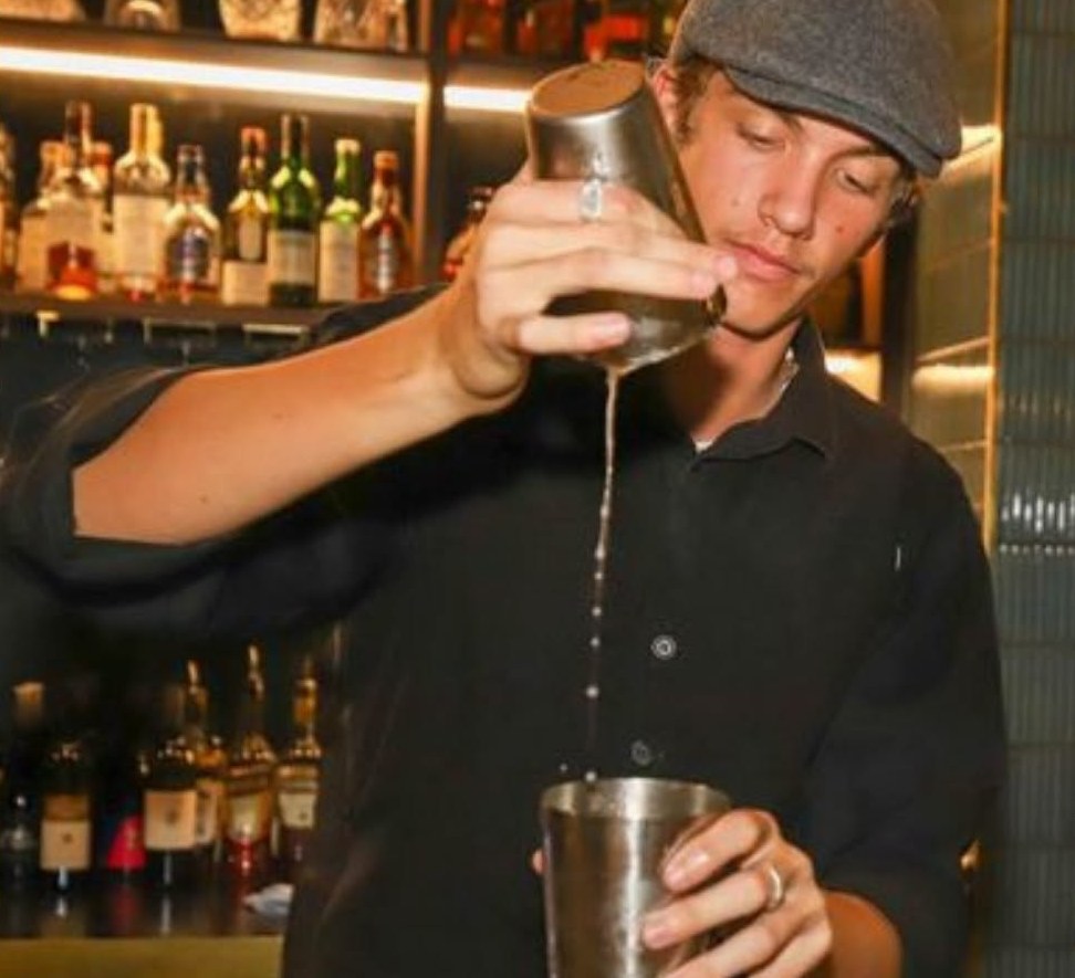 A bartender in a flat cap pouring a shaken cocktail