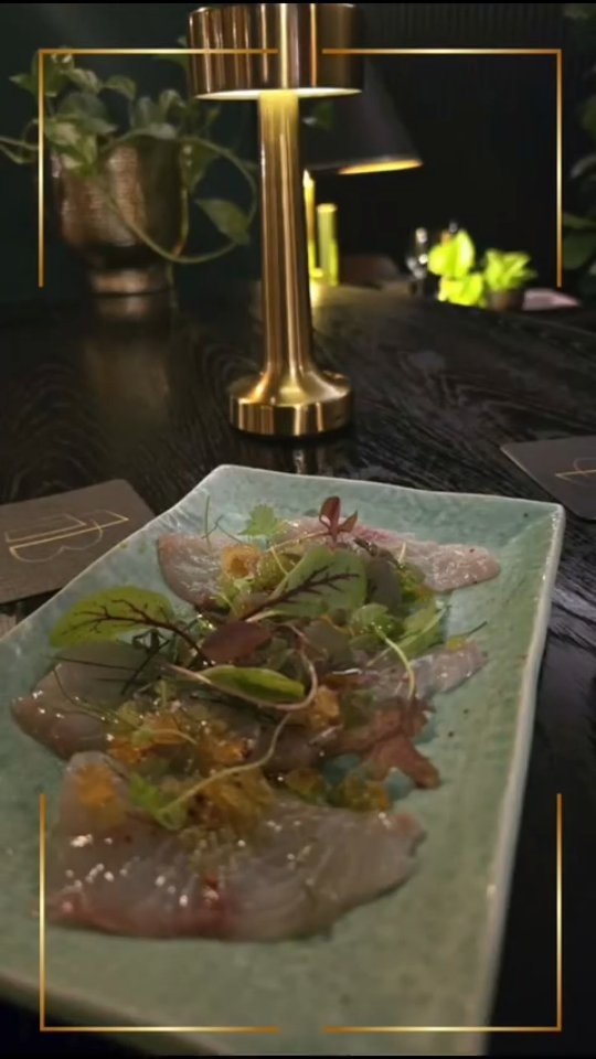 A share plate of raw fish with herbs under a brass table lamp
