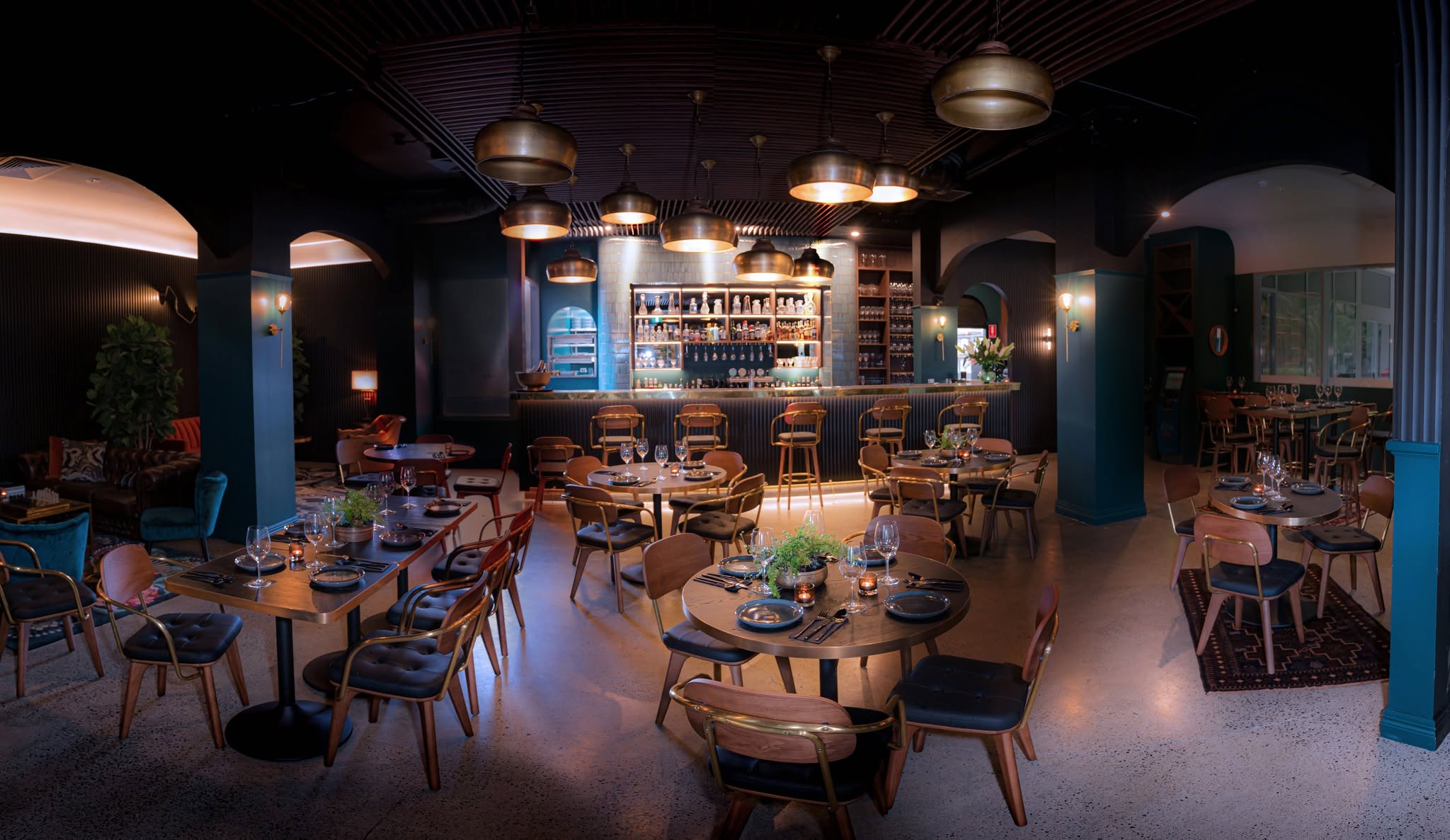 The Brooklyn's dining room: petrol blue walls, brass pendant lights and the bar glowing at the back