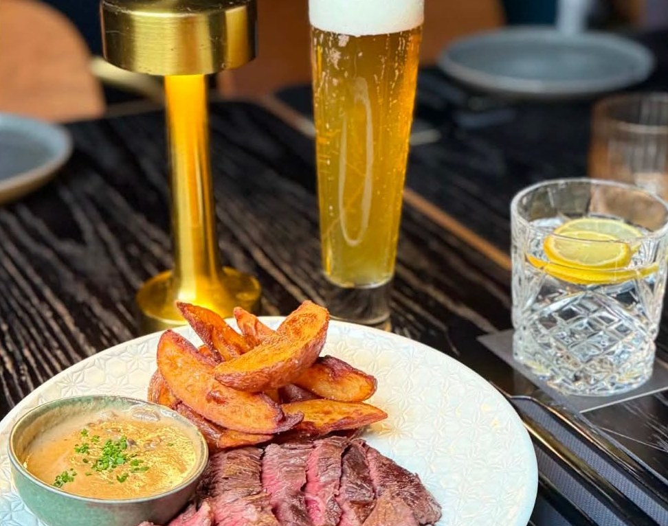 A pint of beer and a gin and tonic beside a steak and wedges